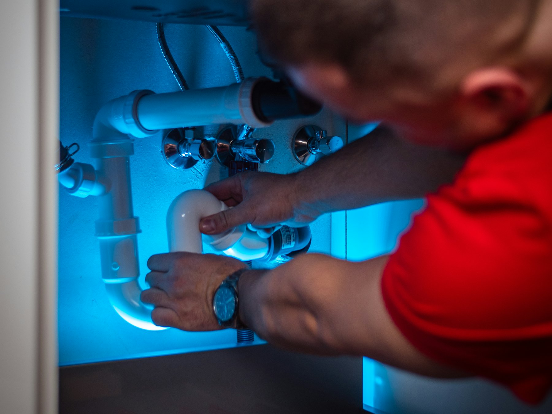 Plumber working on pipework inside a kitchen sink cabinet